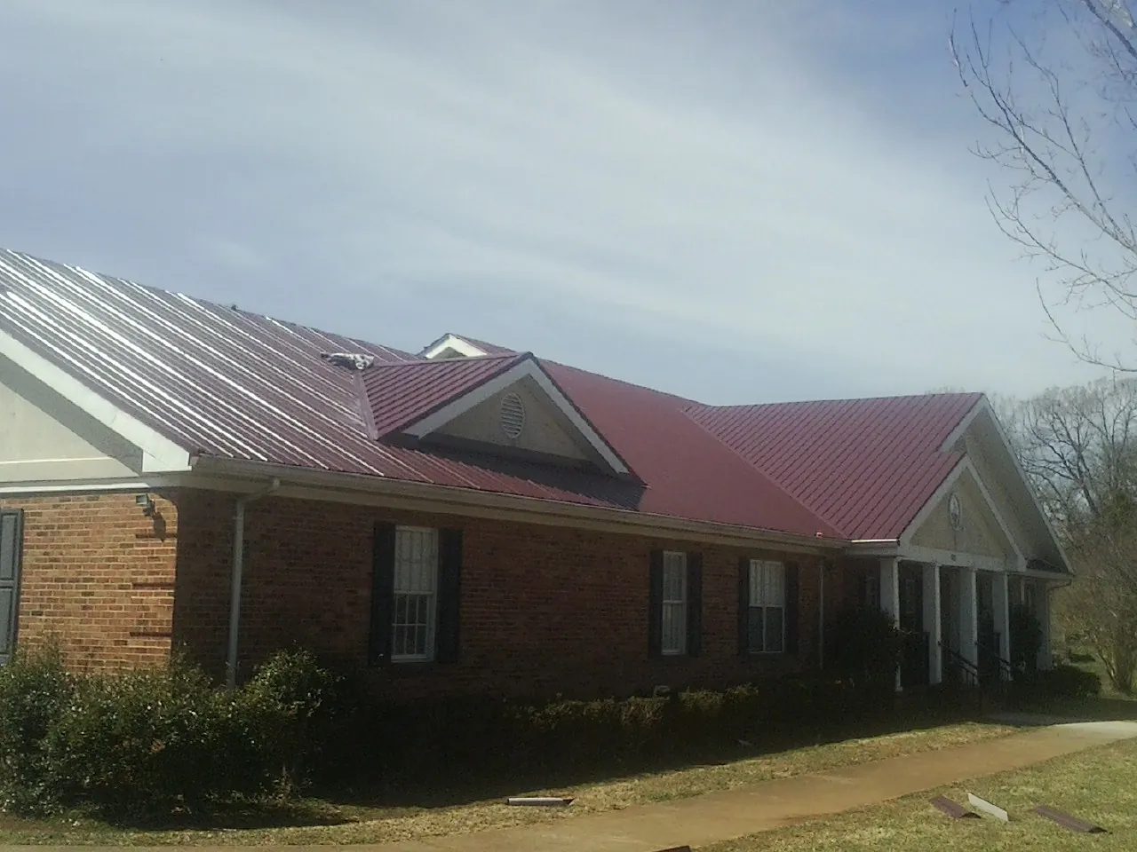 Red metal roof with gabled entries on a long brick building, from a Hail Damage Roof Repair job in Gary