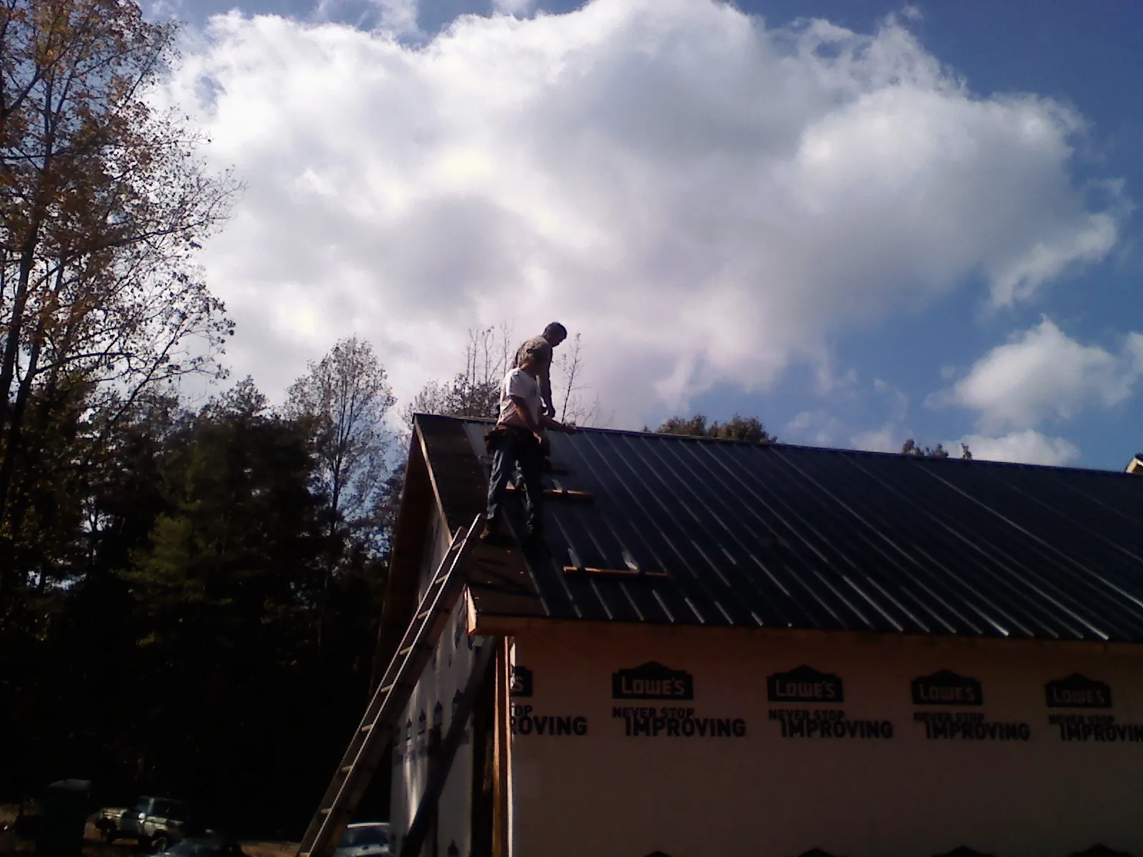 Roofer fastening dark metal panels high against a cloudy sky, from a Roof Inspection job in Gary