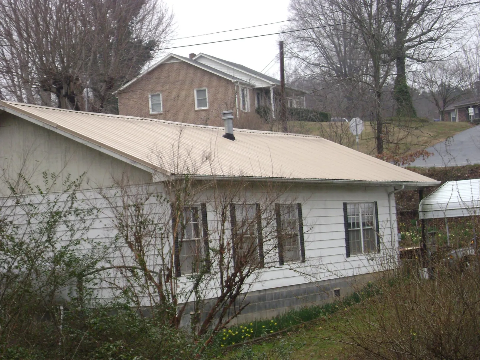 Tan metal roof on a white sided house set into a hillside — Commercial Roofing by Roofing Brothers in Gary