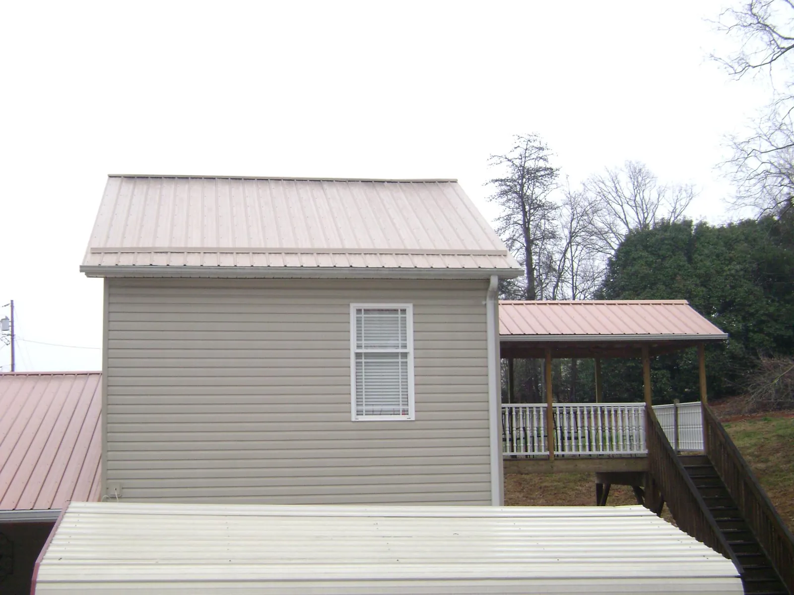 Tan metal roofs on a two story addition and attached porch, from a Roof Replacement job in Gary